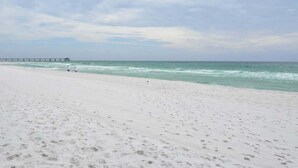 Ein Strand mit weißem Sand und einer Pier, die sich ins Meer erstreckt.