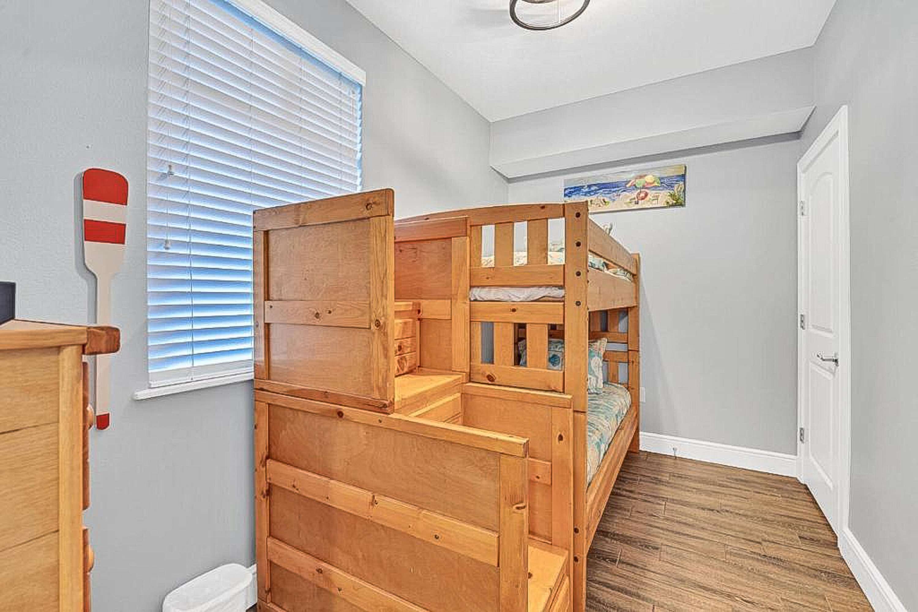 A bunk bed room with a wooden headboard, a window with blinds, and a painting on the wall.