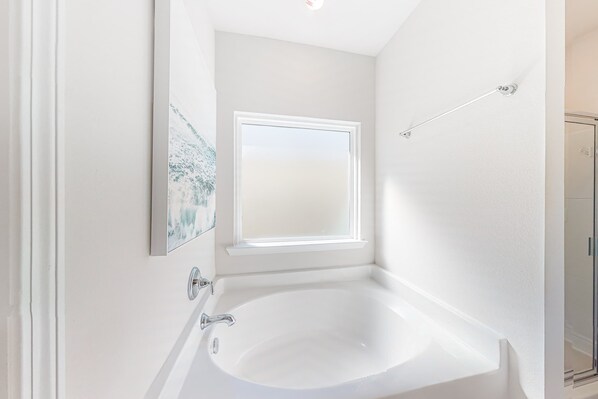 A bathroom with a white bathtub, a window above the tub, and a shower area visible to the right. - Heated community pool, themed kids room, dog friendly Beach, & Relaxing Massage (Port St. Joe)