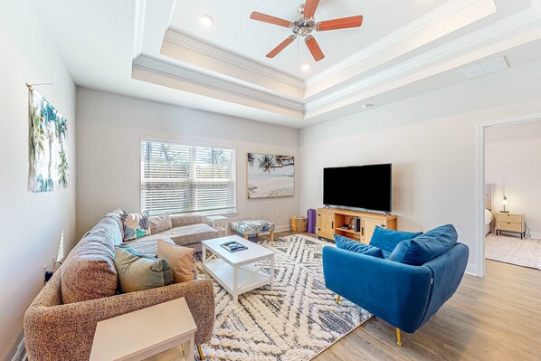 A modern living room with a sectional sofa, a blue armchair, a coffee table, and a flat-screen TV. - Heated community pool, themed kids room, dog friendly Beach, & Relaxing Massage (Port St. Joe)