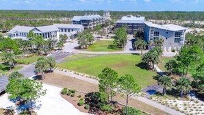 A campus-style building complex with multiple buildings, a central lawn, and surrounding landscaped areas. - Heated community pool, themed kids room, dog friendly Beach, & Relaxing Massage (Port St. Joe)