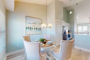 A dining area with a round table, two upholstered chairs, a chandelier, and a painting on the wall. - Dazzling condo near the ocean with private W/D, jetted tub, shared pool, & grill (Mexico Beach)