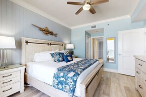 A bedroom with a bed, bedside tables, a ceiling fan, and a door. - gulf front condo steps from the sand with shared pool,hot tub & more (Fort Walton Beach)