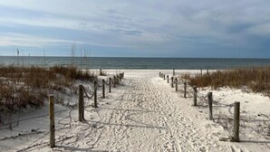 A sandy beach path with wooden posts and chains, leading to the ocean. - Waterfront condo with pool, hot tub, furnished lanai, fireplace & chic furniture (Mexico Beach)