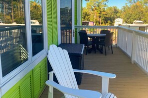 Uma área externa coberta com um deck de madeira, uma cadeira Adirondack branca, uma mesa e cadeiras.