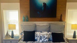 A bedroom with a bed, two nightstands, a painting above the bed, and a window with blinds. - Dog-Friendly Florida Beach House Steps from the Water in Carrabelle (Carrabelle)