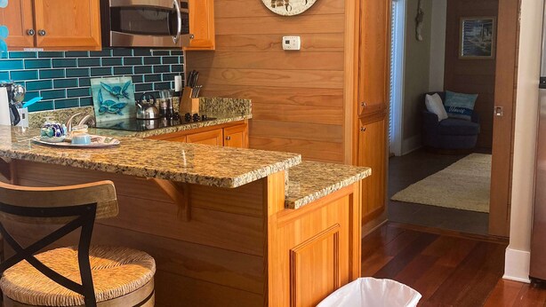 A kitchen with wooden cabinets, a granite countertop, and a stainless steel microwave. - Dog-Friendly Florida Beach House Steps from the Water in Carrabelle (Carrabelle)