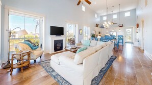 A spacious living room with a fireplace, a large sofa, and a dining area with blue chairs. - Gulf-front home with infinity pool, AC, kayaks, & paddleboard - close to beach (Port St. Joe)