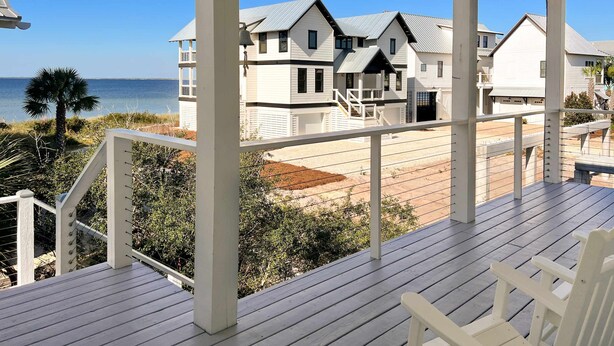 A wooden deck with white railings overlooking a beach and a row of houses with grey roofs. - Gulf-front home with infinity pool, AC, kayaks, & paddleboard - close to beach (Port St. Joe)