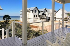 A wooden deck with white railings overlooking a beach and a row of houses with grey roofs. - Gulf-front home with infinity pool, AC, kayaks, & paddleboard - close to beach (Port St. Joe)