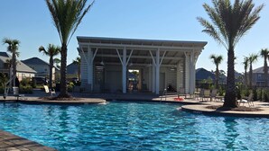 Una piscina con lettini e palme, circondata da edifici e un padiglione coperto.