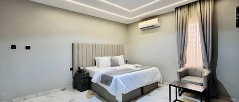A modern bedroom with a bed, bedside table, chair, and an air conditioning unit.