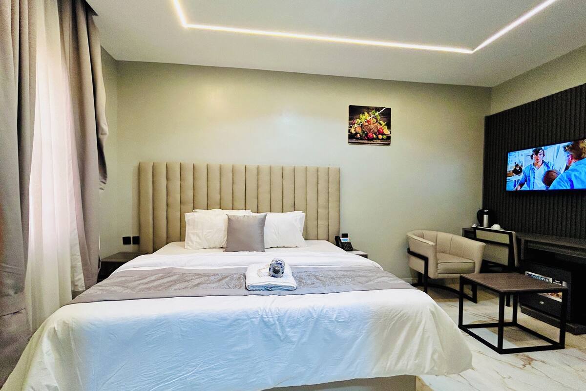 A hotel room with a large bed, a flat-screen TV mounted on the wall, a small desk, and a chair.