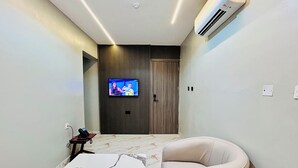 Ein modernes Hotelzimmer mit Marmorboden, einem beigefarbenen Sessel, einem an der Wand montierten Fernseher und einer Klimaanlage.