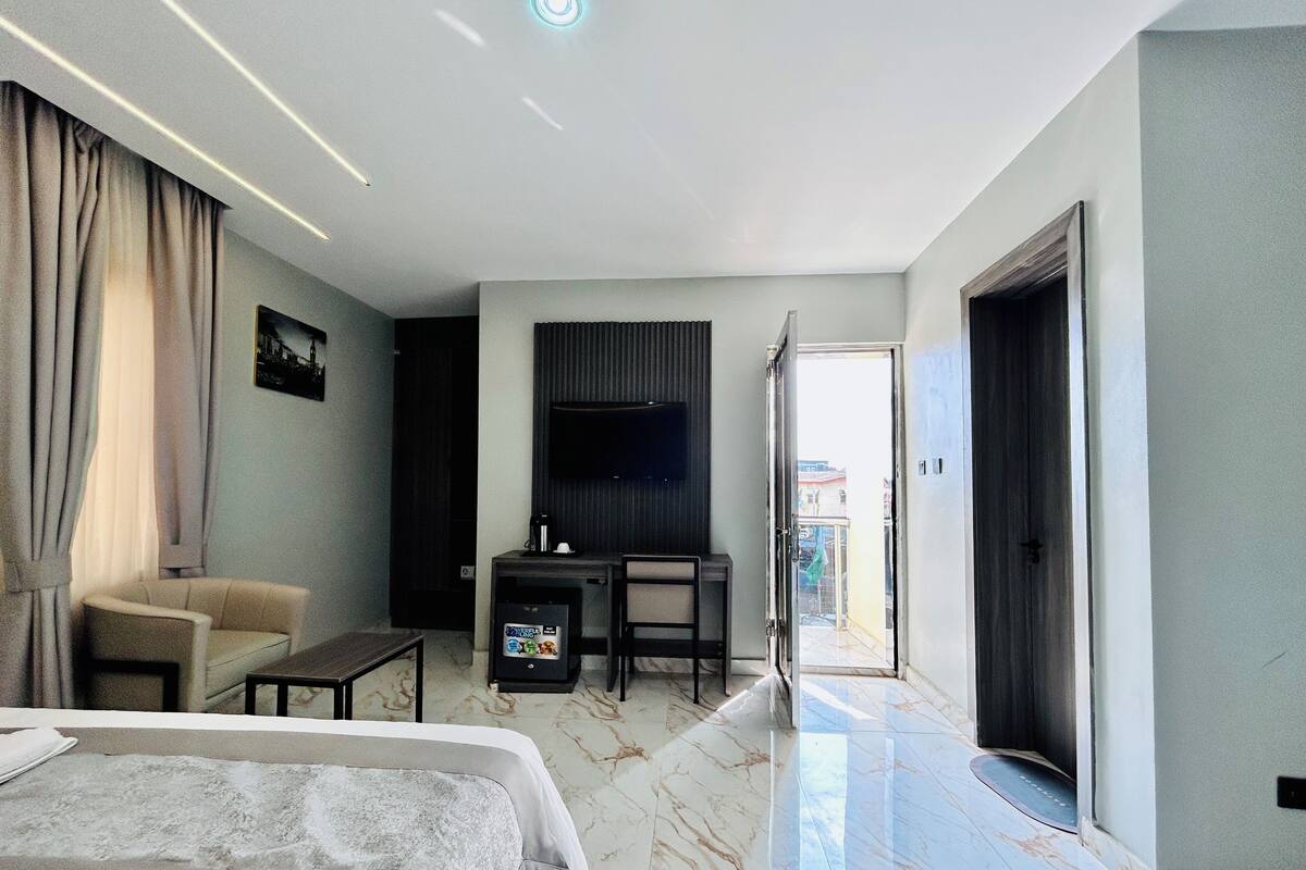 A modern hotel room with a bed, a desk, a chair, a TV, and a balcony.