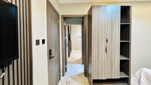 Ein Hotelkorridor mit einem an der Wand montierten Flachbildfernseher, Holztüren und einem eingebauten Wandschrank mit Regalen.