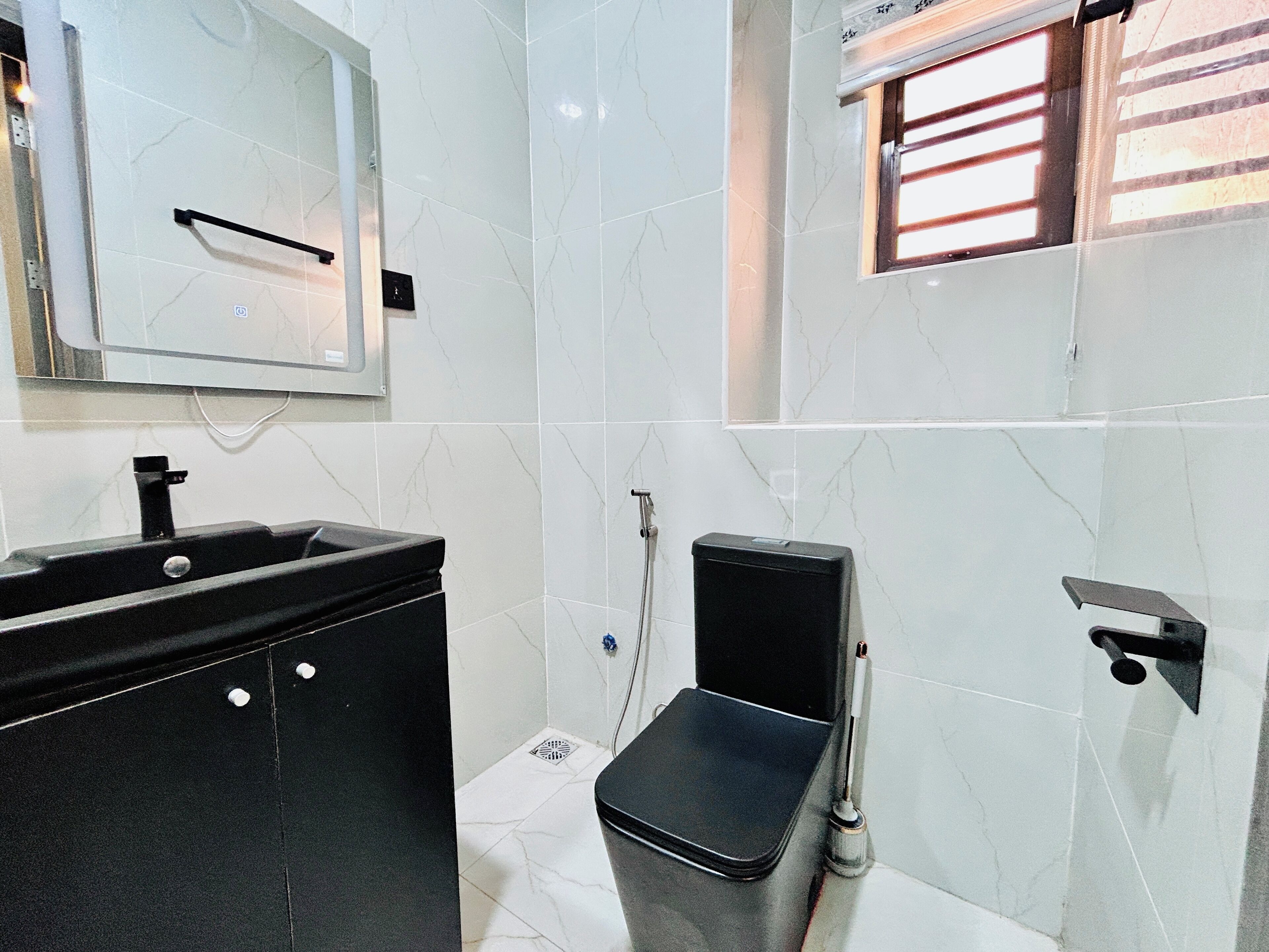 A modern bathroom with a black sink, a mirror, a toilet, and a window with blinds.