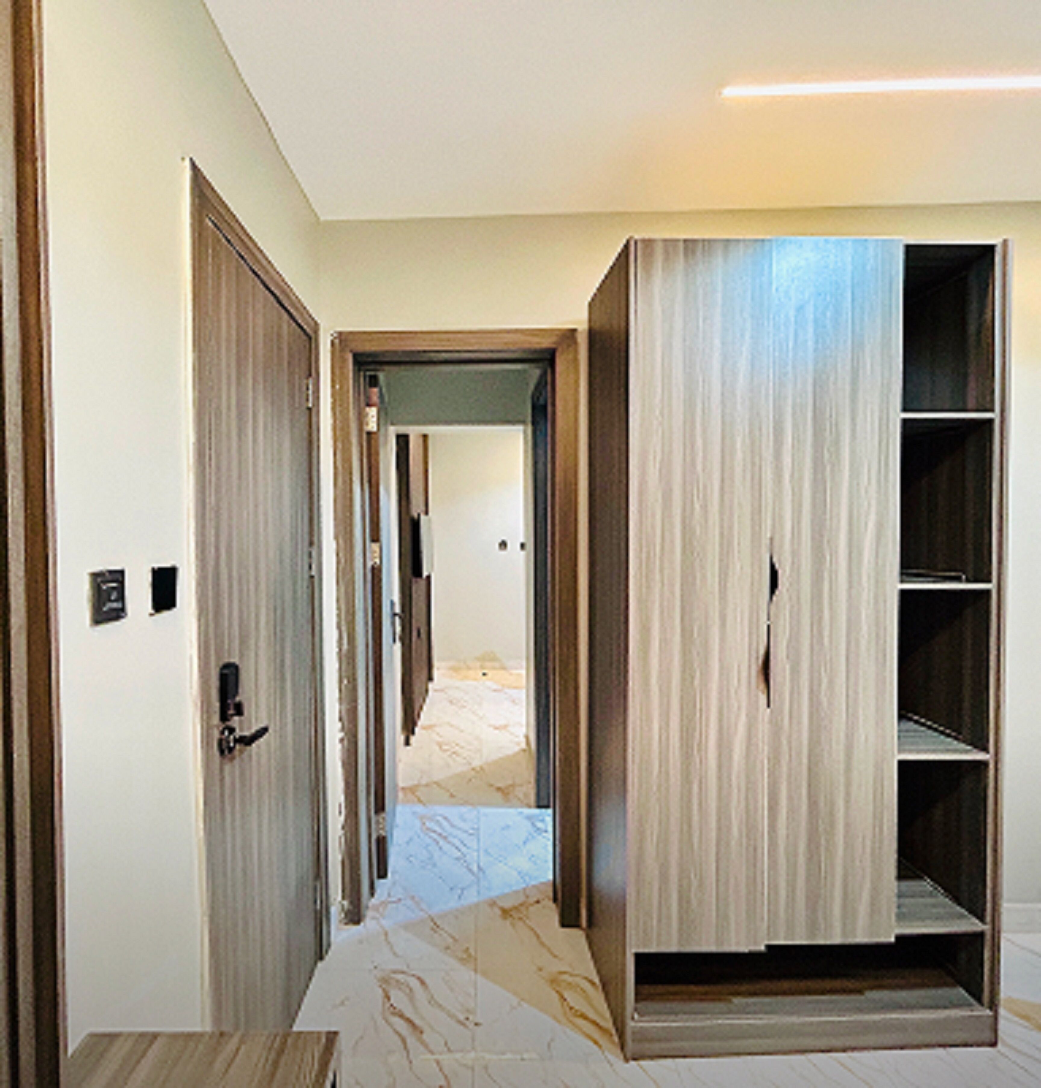 A hallway with a wooden door, a wardrobe with shelves, and a marble floor.