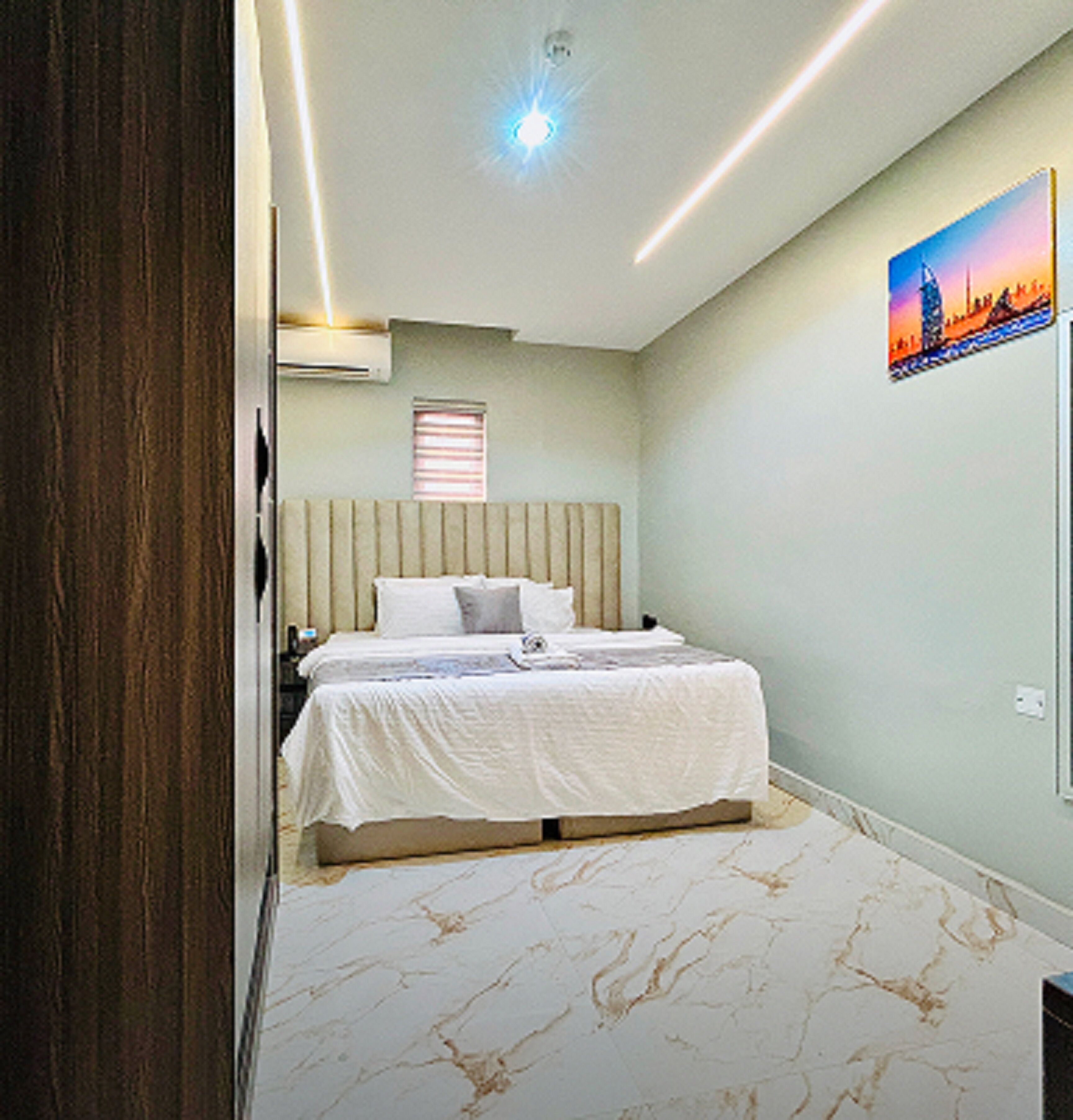 A bedroom with a bed, a window, an air conditioner, and a painting on the wall.