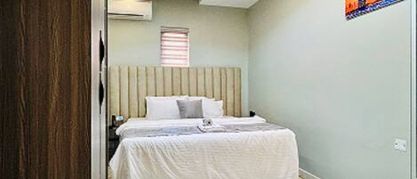 A bedroom with a bed, a window, an air conditioner, and a painting on the wall.