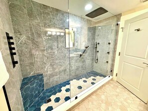 A shower with a glass door, a white door to the right, and a tiled floor with hexagonal patterns. - Spacious condo with bay views, renovated pool, hot tub, & beach access (Miramar Beach)
