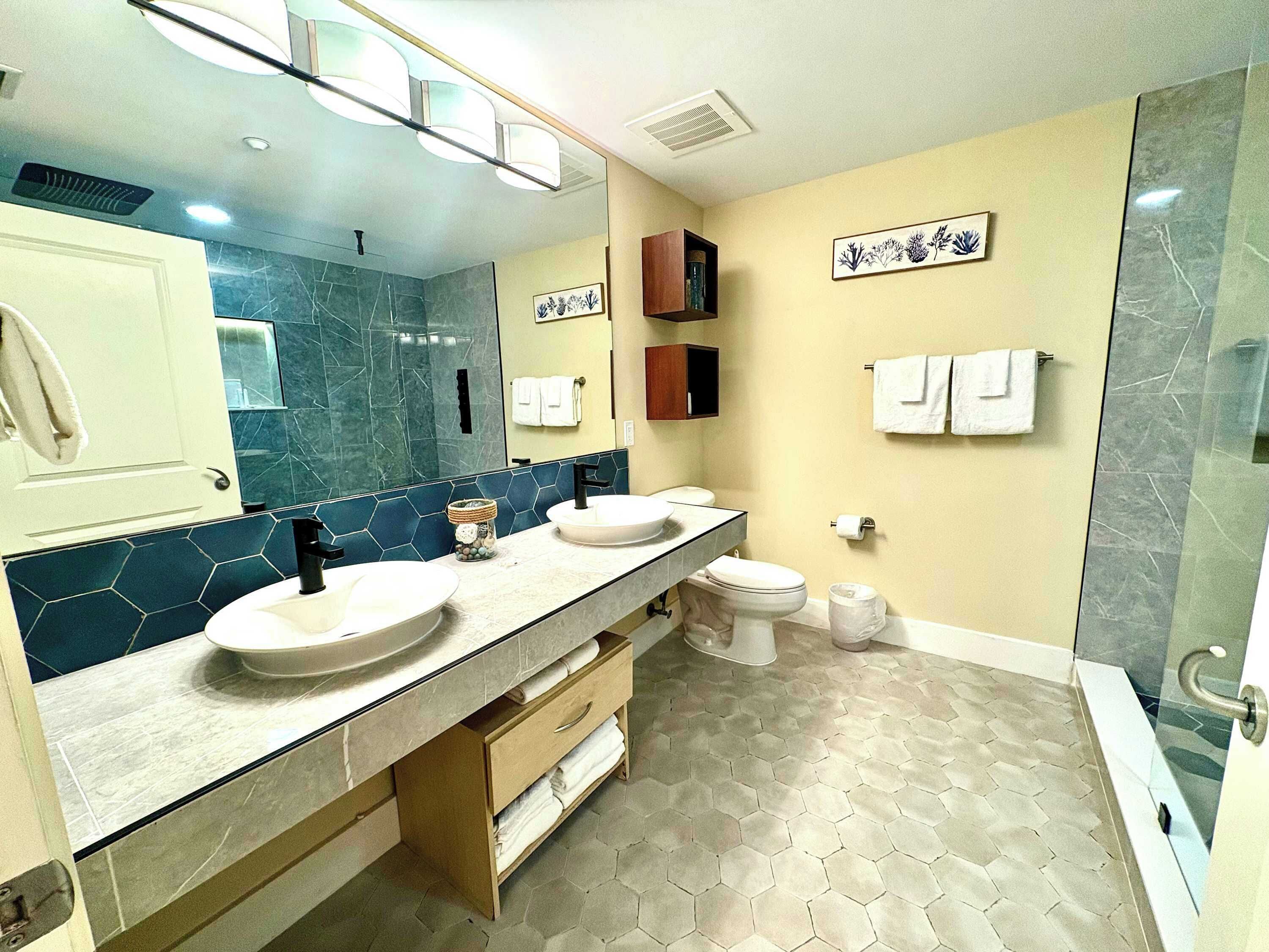 Un baño con dos lavamanos, un inodoro, una ducha y un espejo grande.