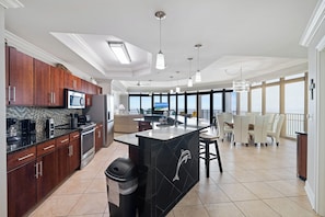 A modern kitchen with dark wooden cabinets, a black island, and a large window overlooking a balcony. - The Oasis at Orange Beach 2501 by Liquid Life (Orange Beach)