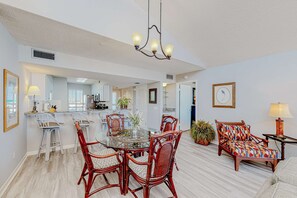 A spacious living area with a glass-top dining table surrounded by wicker chairs, a patterned sofa, and a small side table with a lamp. - 8th Floor condo, Seasonal beach service , Minutes to dining (Miramar Beach)