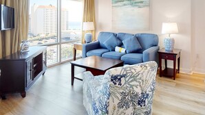 Een moderne woonkamer met een blauwe bank, een fauteuil met bloemenprint, een houten salontafel en een televisie op een kast.