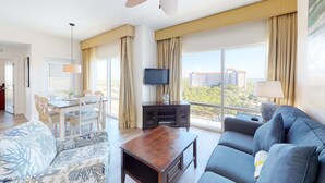 Een moderne hotelkamer met een groot raam, een plafondventilator, een flatscreen-tv, een zithoek met een tafel en stoelen, en een bank.