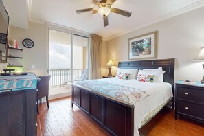 Ein Hotelzimmer mit Bett, Schreibtisch, Sessel, Deckenventilator, Fenster und einem Bild an der Wand.