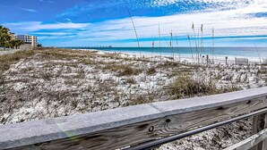 A beach with a wooden railing, sandy dunes, and a distant pier. - 4th-Floor Azure Condo with Free WiFi, Beach Service, Gulf View, Shared Pool,Hot Tub (Fort Walton Beach)