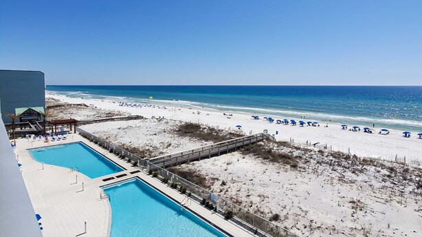 A beach view with a swimming pool and beach umbrellas. - Blu 507 - Luxurious gulf front condo with private balcony, shared pool & beach access (Fort Walton Beach)