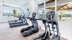 A gym with treadmills, large windows, and a view of palm trees and buildings. - Blu 507 - Luxurious gulf front condo with private balcony, shared pool & beach access (Fort Walton Beach)