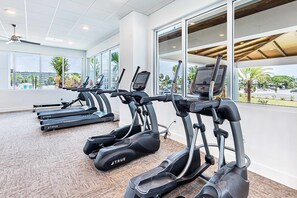 A gym with treadmills, large windows, and a view of palm trees and buildings. - Blu 507 - Luxurious gulf front condo with private balcony, shared pool & beach access (Fort Walton Beach)
