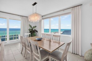 A dining area with a view of the ocean, a chandelier, and a plant. - Blu 507 - Luxurious gulf front condo with private balcony, shared pool & beach access (Fort Walton Beach)
