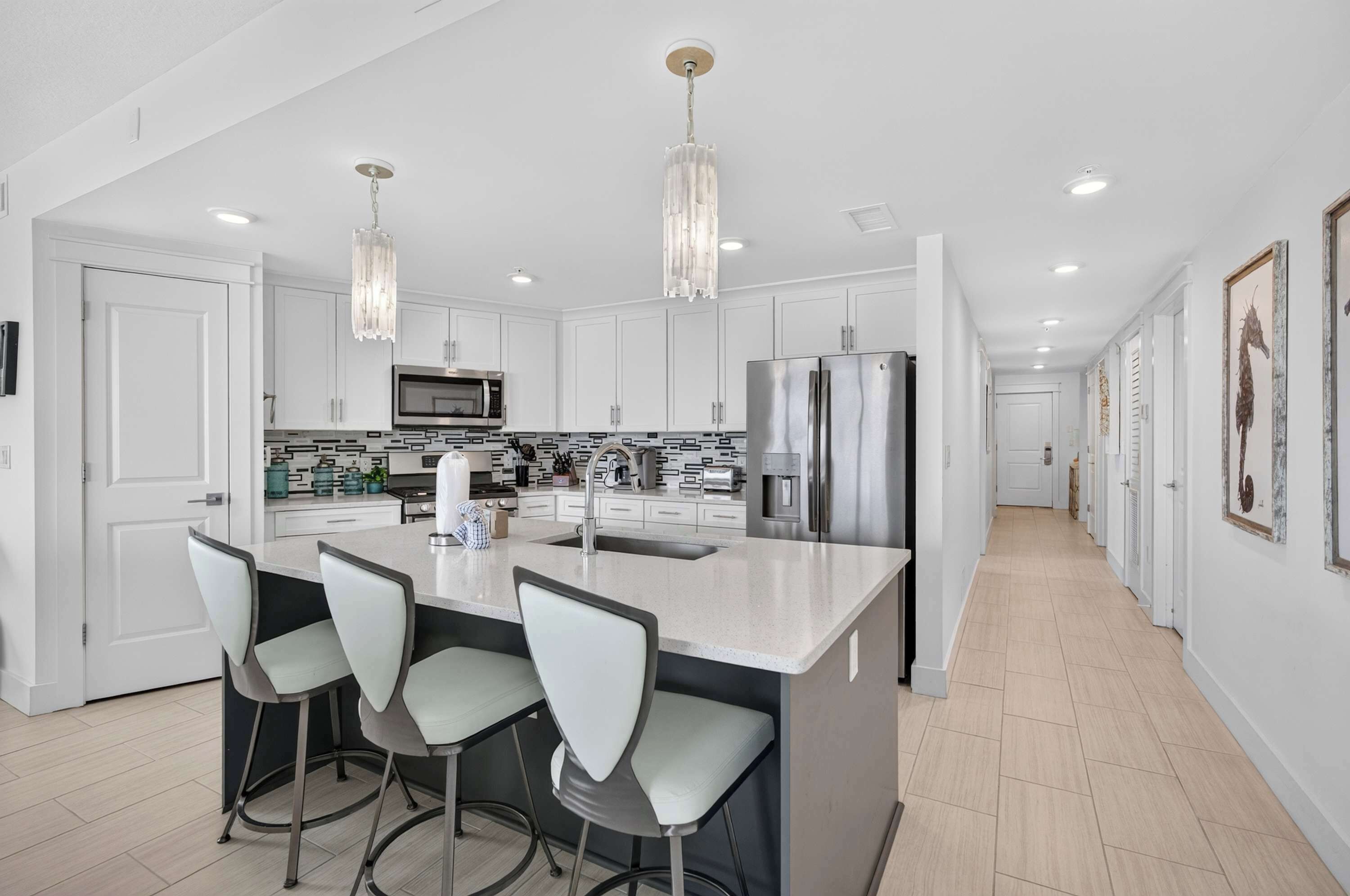 A modern kitchen with a central island, bar stools, stainless steel appliances, and pendant lighting.