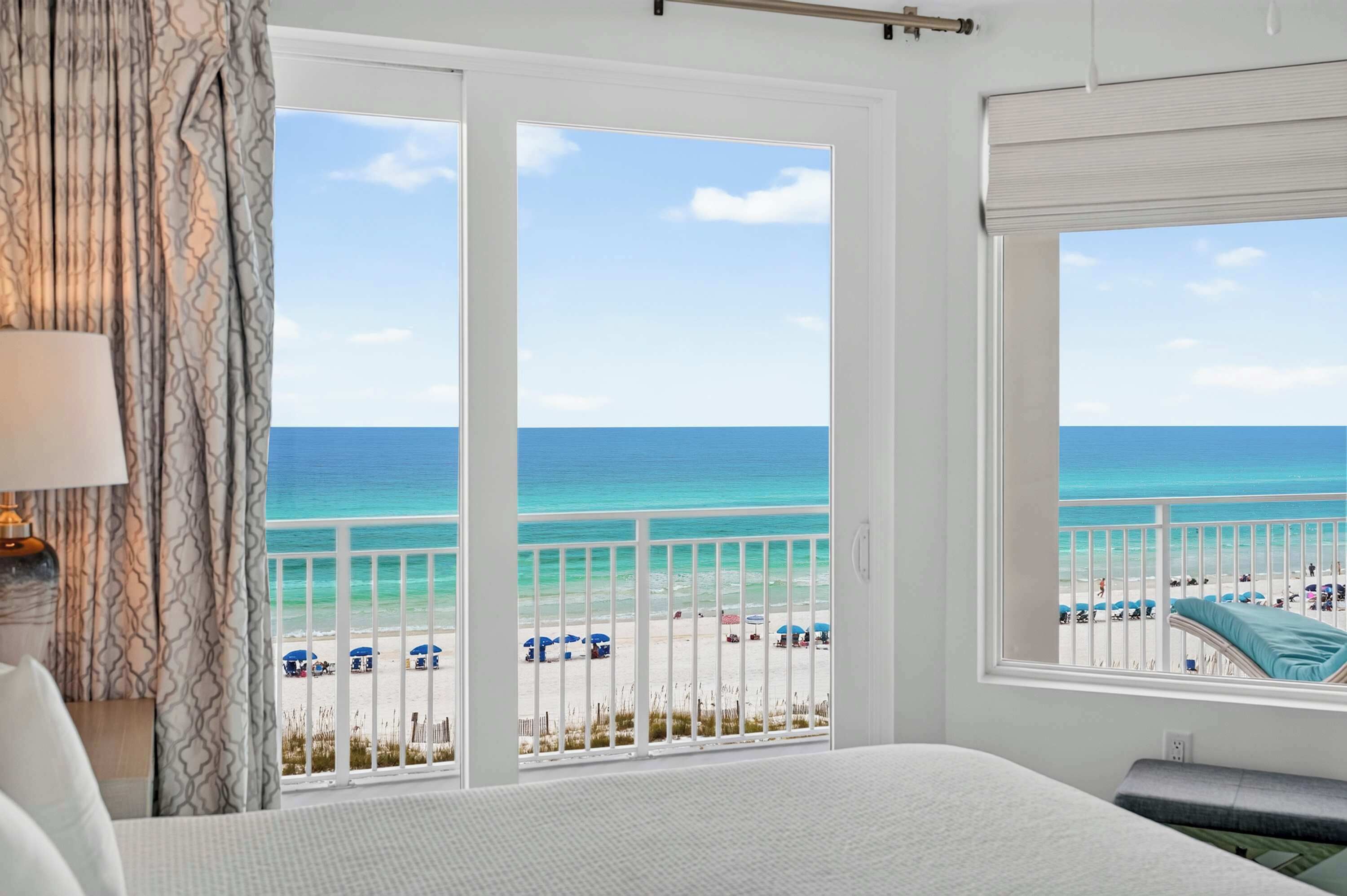 A hotel room with a large window offering a view of the beach and ocean.