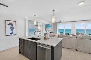 A modern kitchen with a dishwasher, a large island, and a view of the ocean. - Blu 507 - Luxurious gulf front condo with private balcony, shared pool & beach access (Fort Walton Beach)