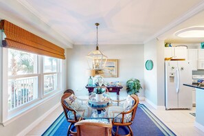 A dining area with a glass table, wicker chairs, a hanging light fixture, and a view of the outdoors through large windows. - Sunny nautical condo with on-site hot tub, pool, & gym - internet, W/D, & AC (Mexico Beach)