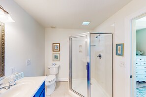 A bathroom with a glass-enclosed shower, a white sink with blue cabinets, and a toilet. - Sunny nautical condo with on-site hot tub, pool, & gym - internet, W/D, & AC (Mexico Beach)