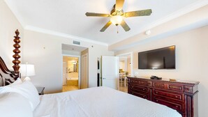 Ein Hotelzimmer mit einem großen Bett, einer Holzkommode, einem Deckenventilator und einem flachbildfernseher an der Wand.