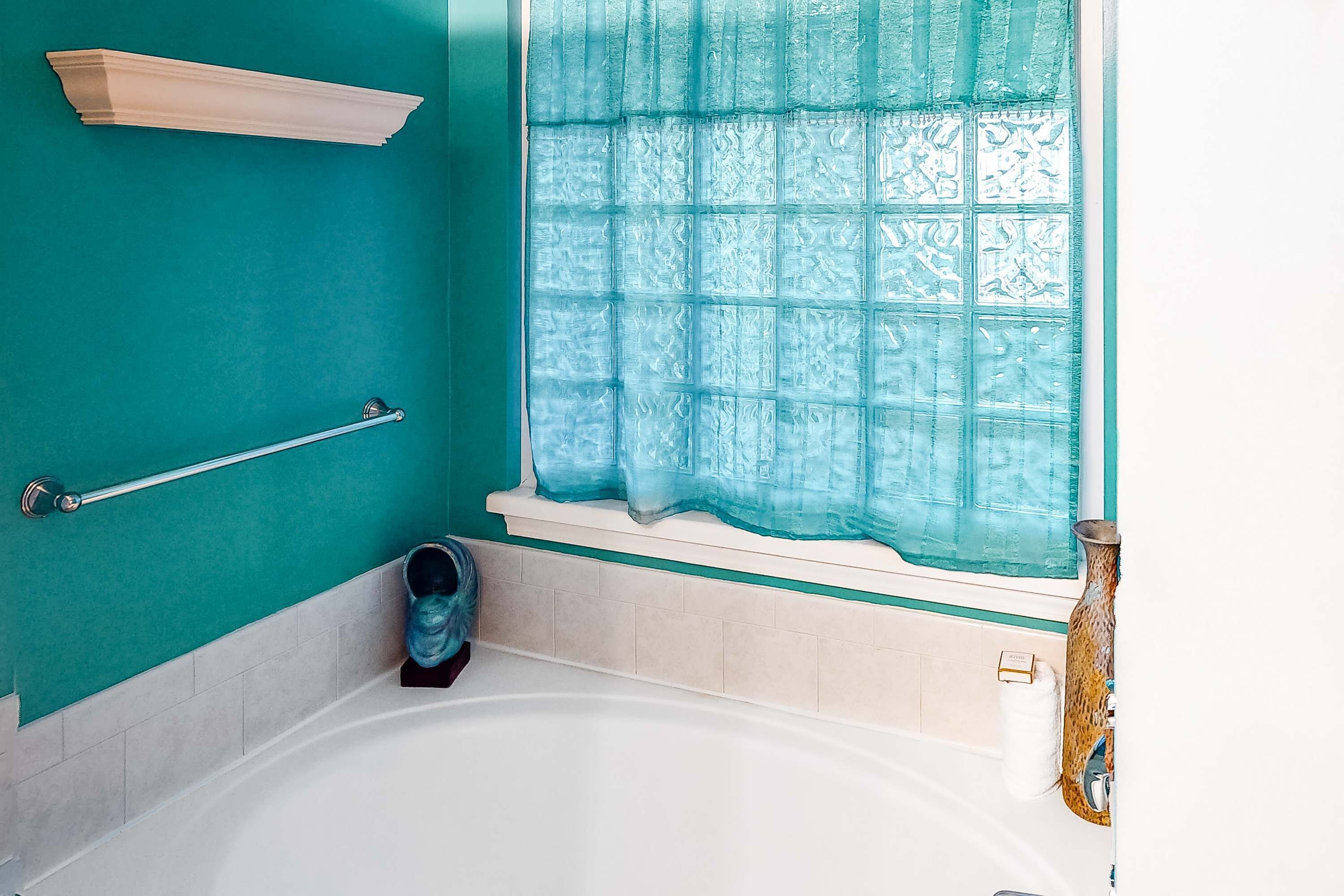 A bathroom with a bathtub, a window with a patterned curtain, a towel rack, and a wooden shelf.