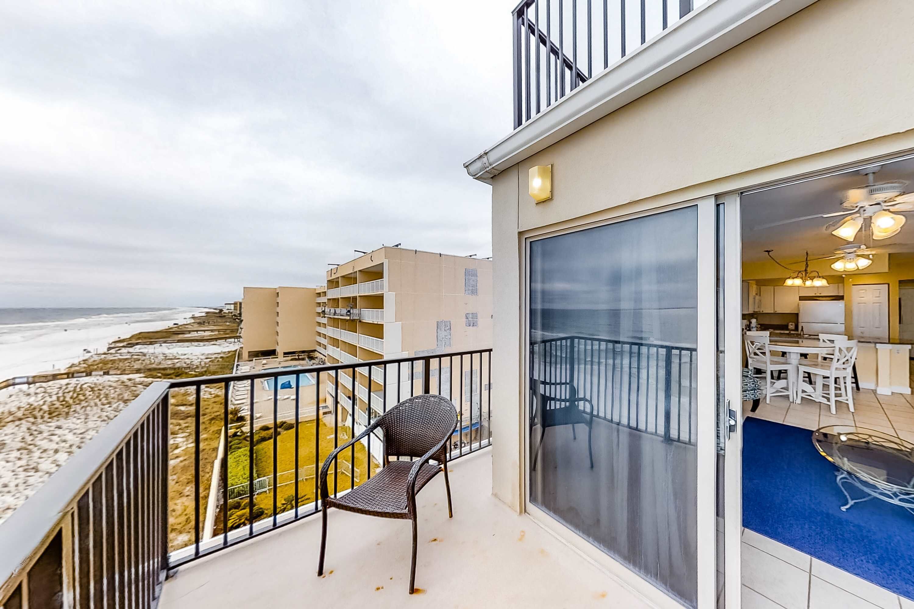 A balcony with a chair, a view of the beach, and a glimpse of the interior with a dining area.