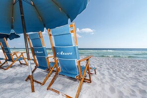 Sillas de playa con sombrillas identificadas con el nombre "Azure" en una playa arenosa.