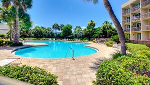 Una piscina rodeada de palmeras y sillones de descanso, con un edificio al fondo.