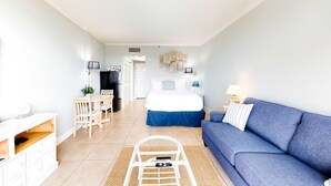 Una habitación moderna y bien iluminada con una cama, un sofá azul, una mesa de comedor y una pequeña cocina.