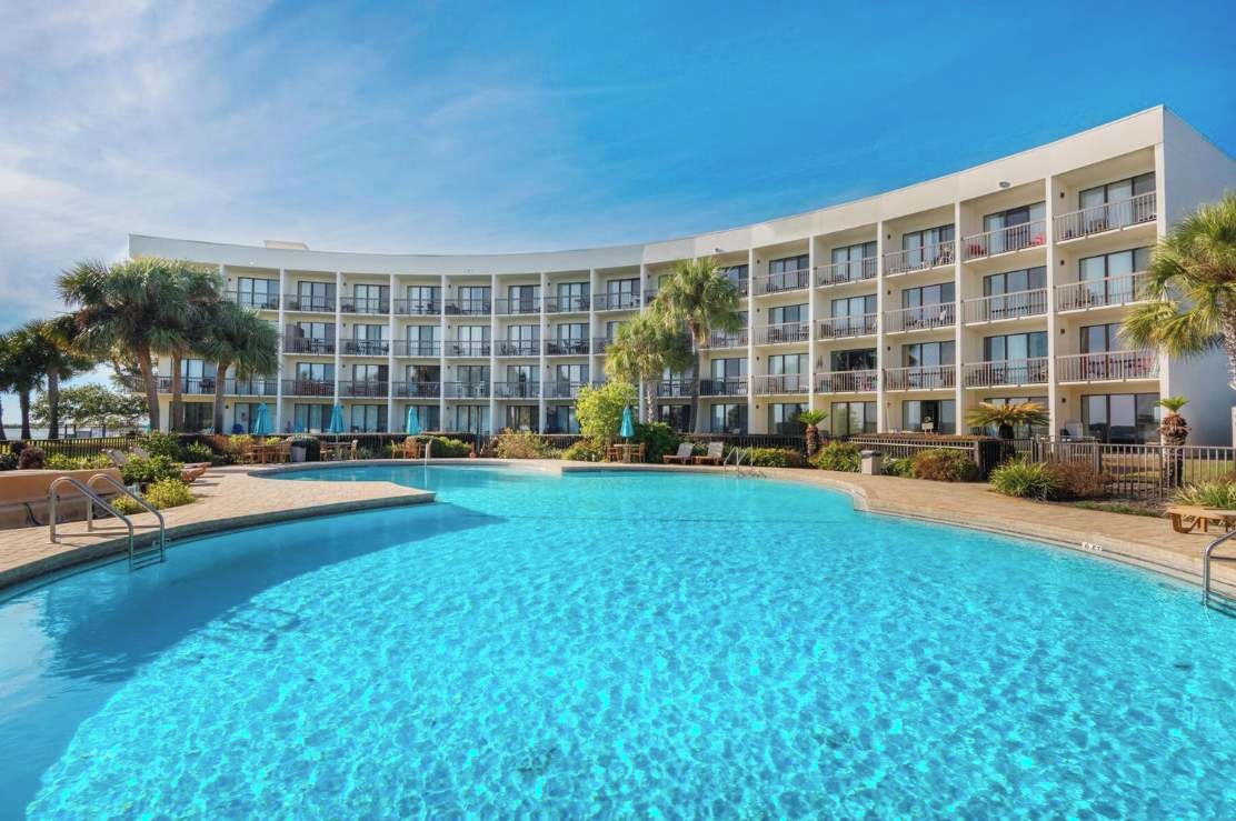 Un hotel con piscina, varios balcones y palmeras.