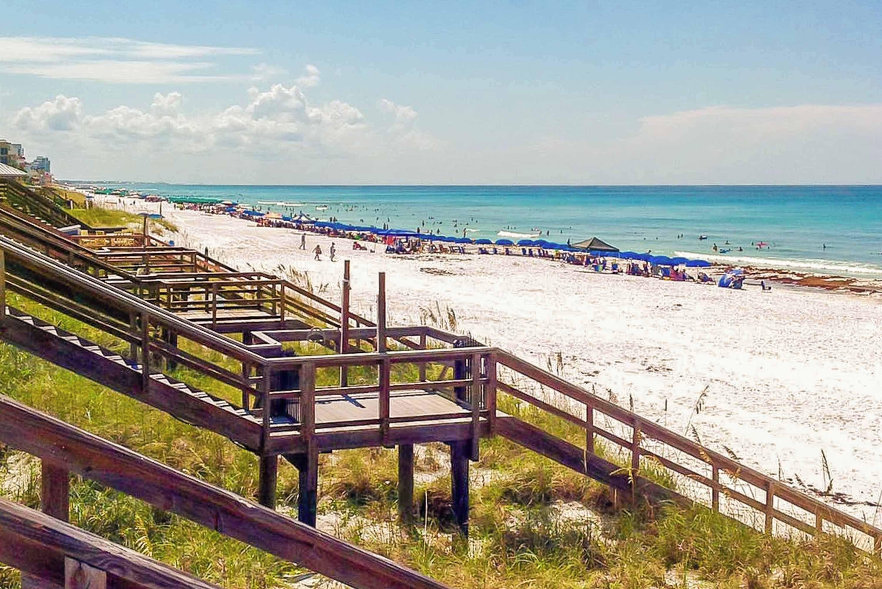 Une plage avec des passerelles en bois menant au rivage, une plage de sable et un ciel bleu clair.