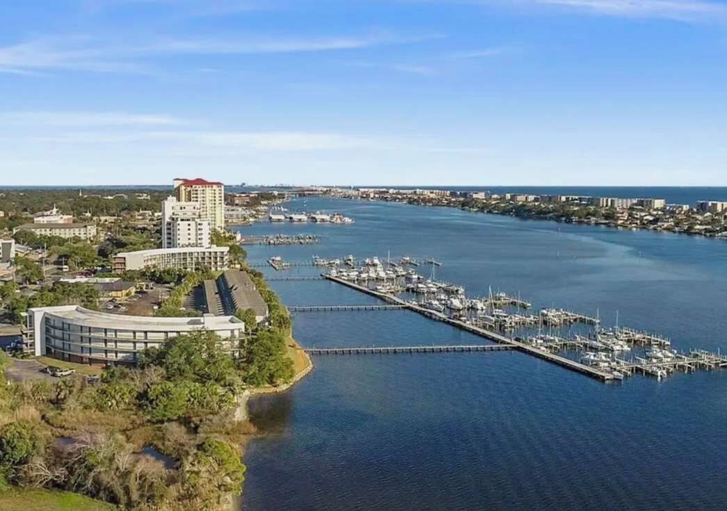 Un port de plaisance avec de nombreuses jetées et des bateaux, un grand bâtiment à la façade incurvée et une vue lointaine sur les contours d’une ville.